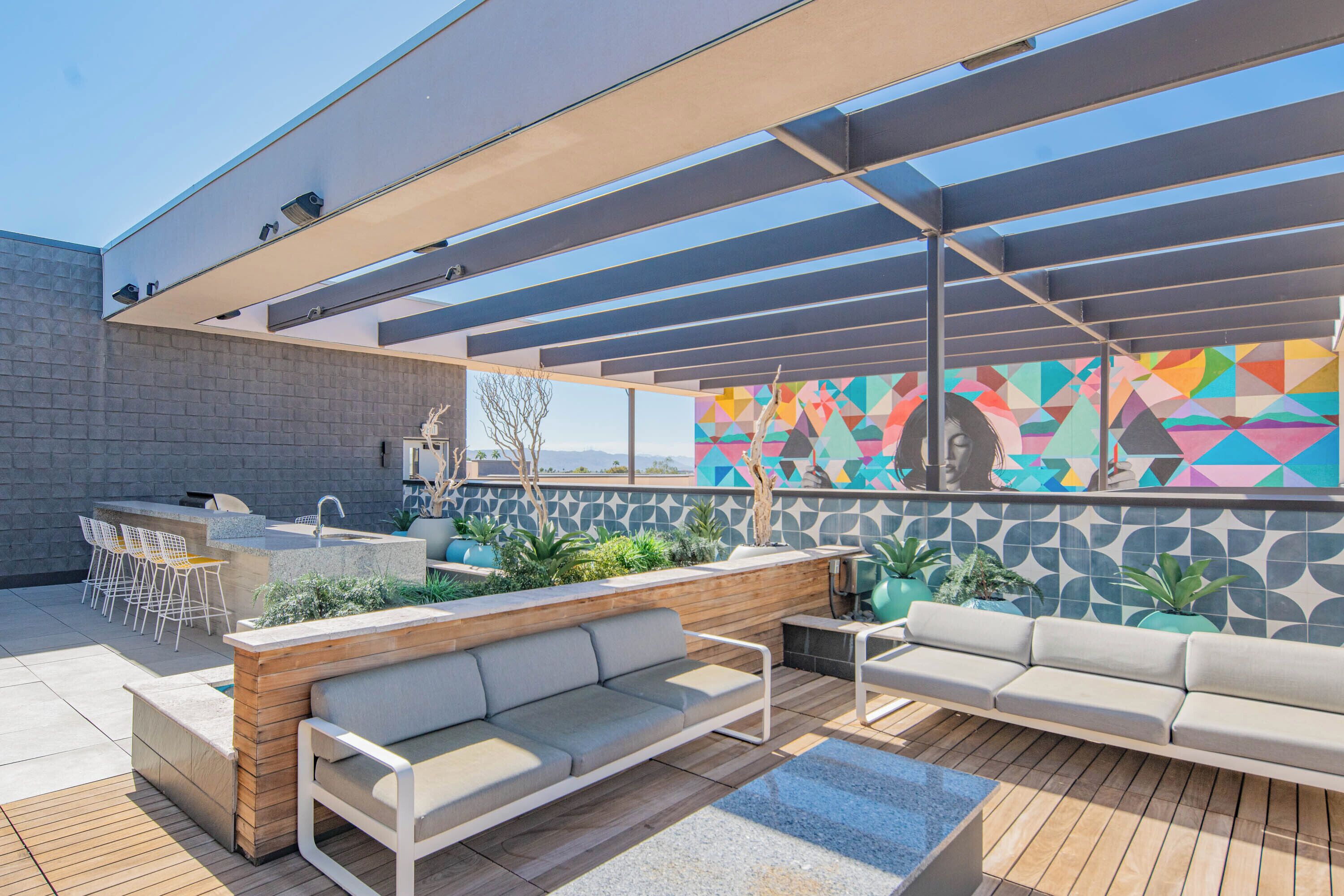 An outdoor patio with a wooden deck, two sofas, a small table, and a bar area with chairs.