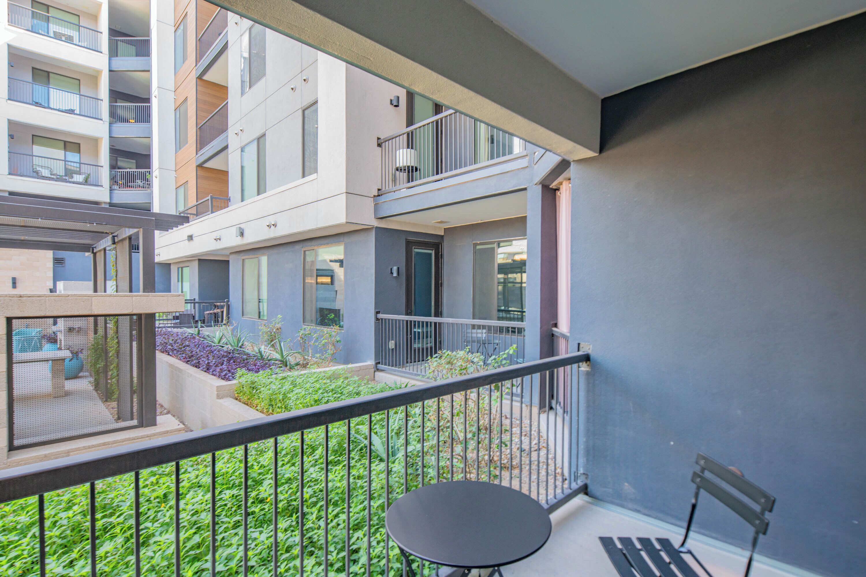 A balcony with a table and a bench, surrounded by greenery and a view of adjacent buildings.