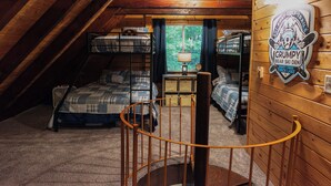 Un dormitorio acogedor en el ático con literas, una escalera de madera y vistas al bosque a través de una ventana.