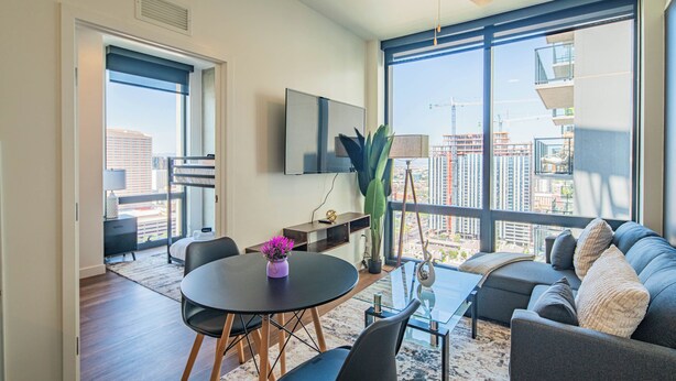 A modern living room with a dining table, sofa, and large windows offering a city view. - ROVE LIVING/KB - Joy on 4th (Phoenix)