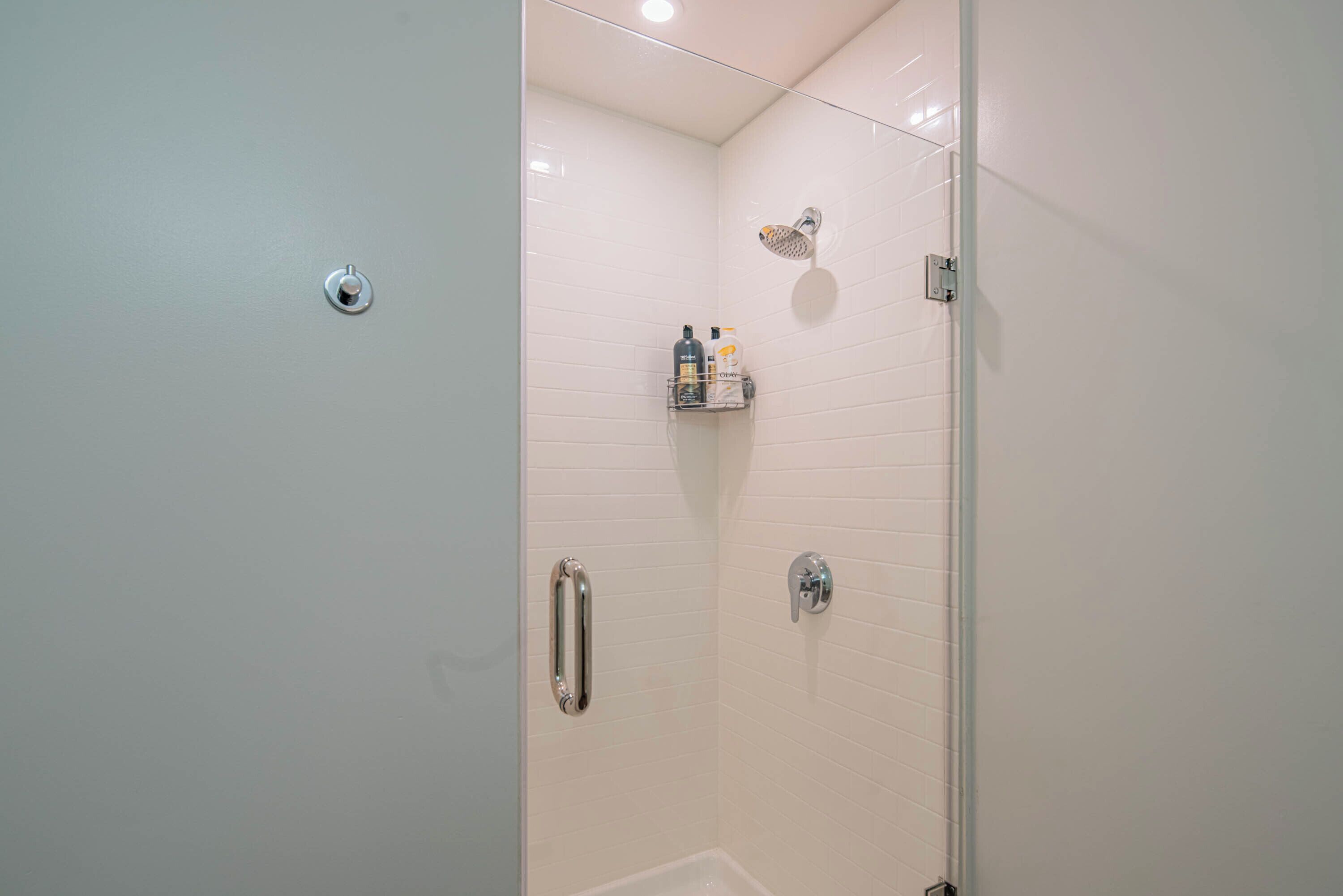 Un bagno moderno con box doccia in vetro, pareti rivestite di piastrelle bianche e uno scaffale a incasso con articoli da toilette.