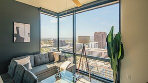 A modern living room with a large window, a ceiling fan, a sofa, a coffee table, and a floor lamp. - ROVE LIVING/KB - Joy on 4th (Phoenix)