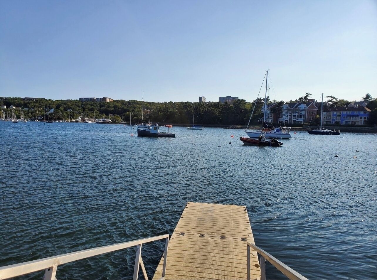 Un port de plaisance avec plusieurs bateaux amarrés, une jetée en bois et des bâtiments en arrière-plan.