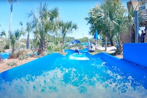 Un toboggan aquatique se terminant dans une piscine bleue, entouré de palmiers et sous un ciel dégagé.