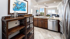 A modern kitchen with wooden cabinetry, a stainless steel refrigerator, and a large window offering a view of the outdoors. - Waters Edge 304 • Luxury 3BR 3BA, Balcony, Large Pool, Covered Parking, Free Bch Service (Fort Walton Beach)