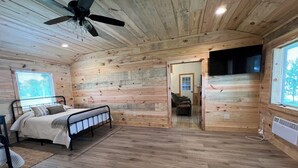 Ein Schlafzimmer einer Holzhütte mit Bett, Stuhl, Deckenventilator und Fenster.