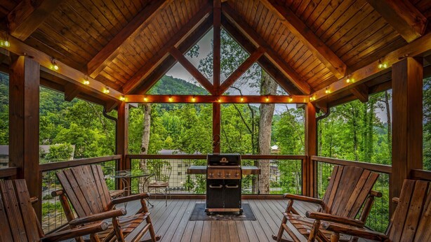 A wooden deck with a barbecue grill, two rocking chairs, and a glass table.