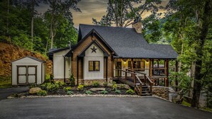 A rustic cabin with a stone chimney, a wooden deck, and a small porch.