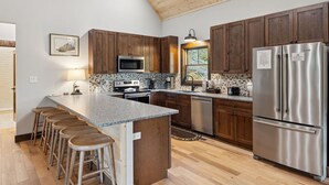 A kitchen with wooden cabinets, a stainless steel refrigerator, a microwave, and a large island with stools.