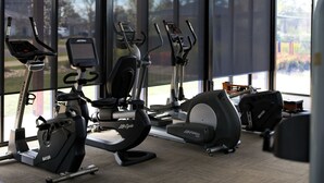Un gimnasio con equipo de cardio, ventanas amplias y vistas al exterior.