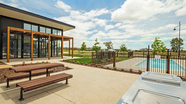 Un patio al aire libre con bancos, piscina y un edificio moderno con grandes ventanales.