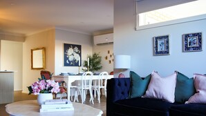 Una sala de estar moderna con un sofá azul oscuro, una mesa de centro blanca y un comedor con sillas y una mesa blancos.