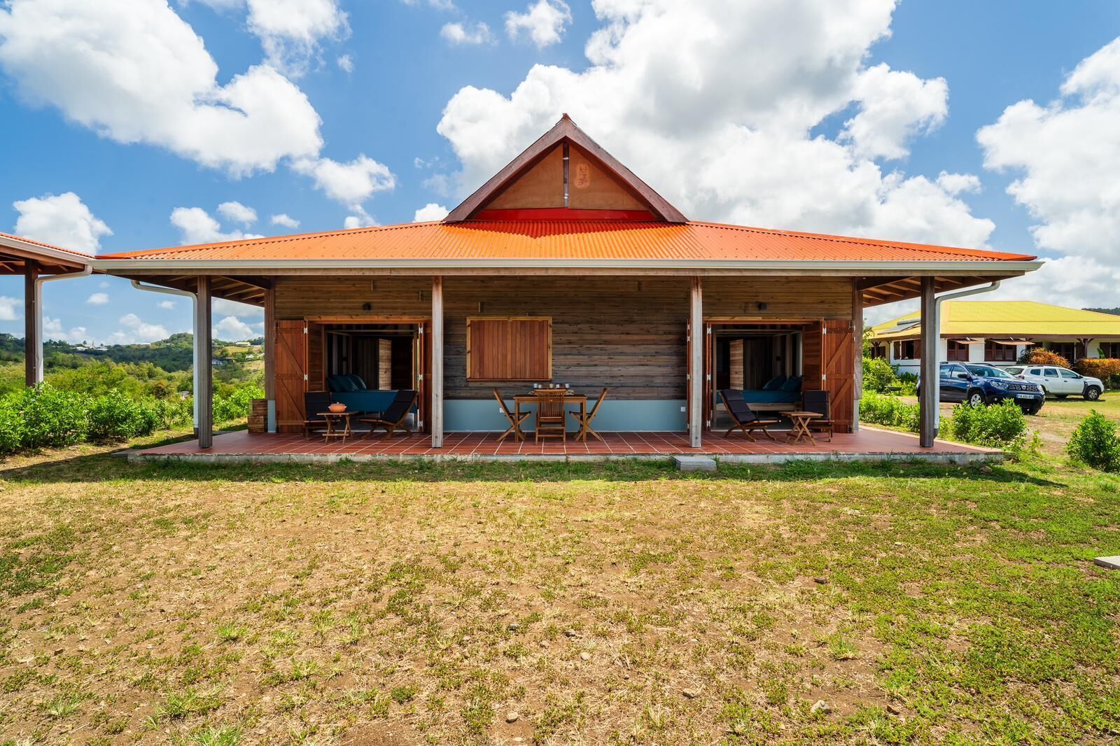 A wooden cabin with a red roof, a covered patio with seating, and a view of the surrounding landscape.
