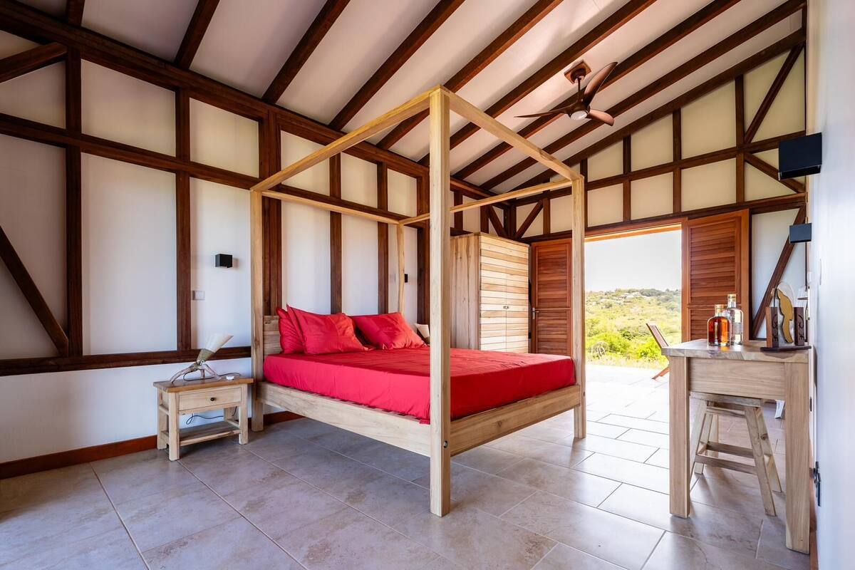 A bedroom with a four-poster bed, a wooden desk, and a view of the outdoors.