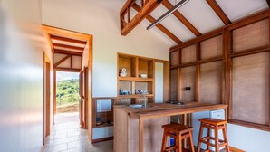 A kitchen with wooden beams, a central island, bar stools, and built-in shelves. - Ecolodges Puyferrat (Le Marin)