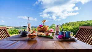 A wooden table set with breakfast items, including eggs, bread, and a coffee pot, overlooking a scenic landscape. - Ecolodges Puyferrat (Le Marin)