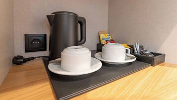 Une chambre d’hôtel avec une machine à café noire, deux tasses blanches sur un plateau noir, une prise électrique et une boîte de Nesquik.