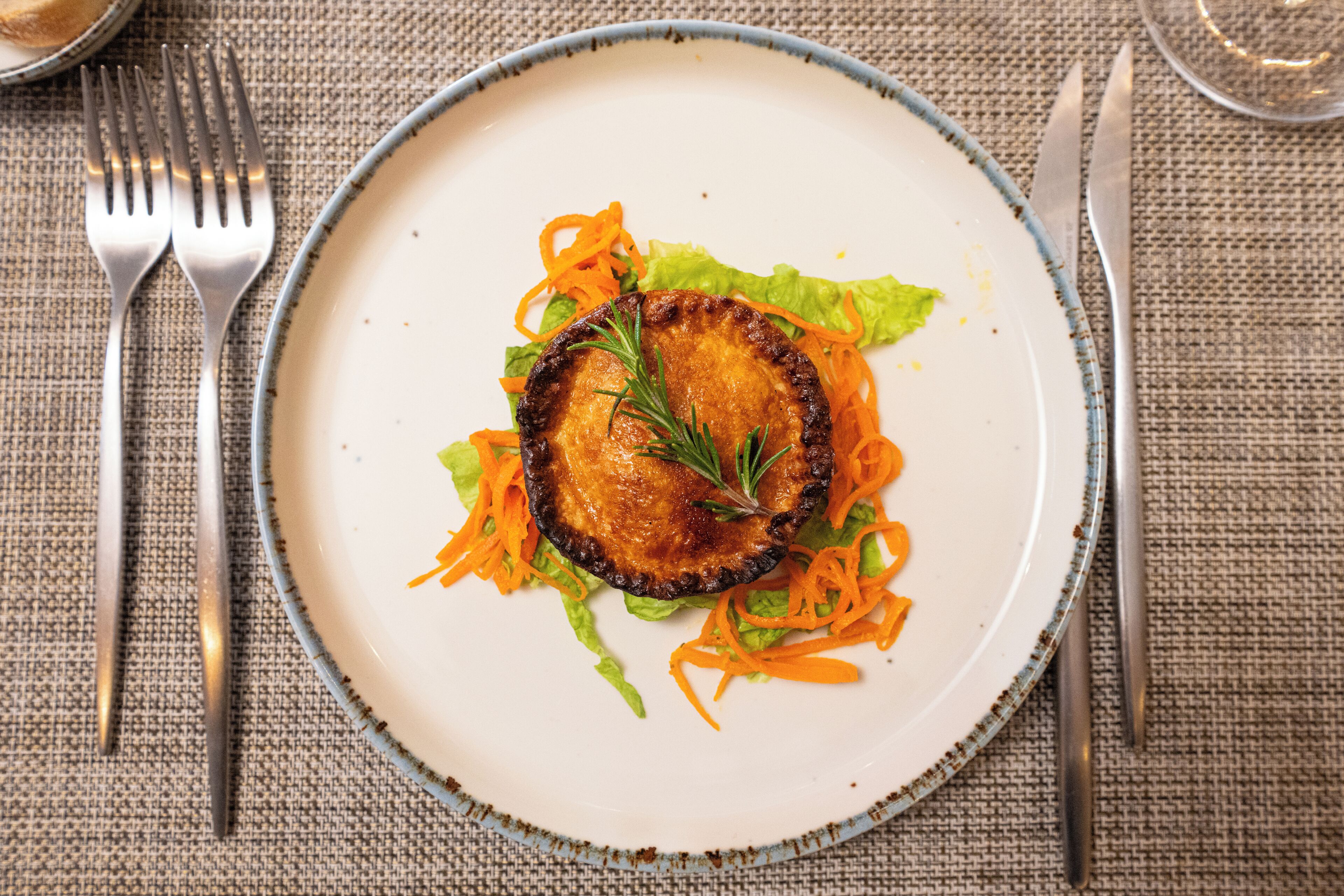 A plate with a slice of meat, carrot shreds, and lettuce on a textured tablecloth.
