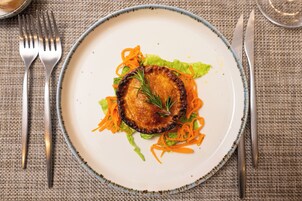 Un plato con una porción de carne, zanahoria rallada y lechuga sobre un mantel texturizado.