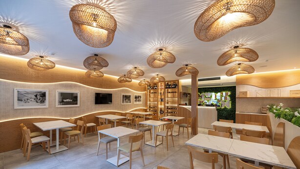 Ein modernes Restaurant mit Holztischen und -stühlen, gewobenen Pendelleuchten und einer Bar.