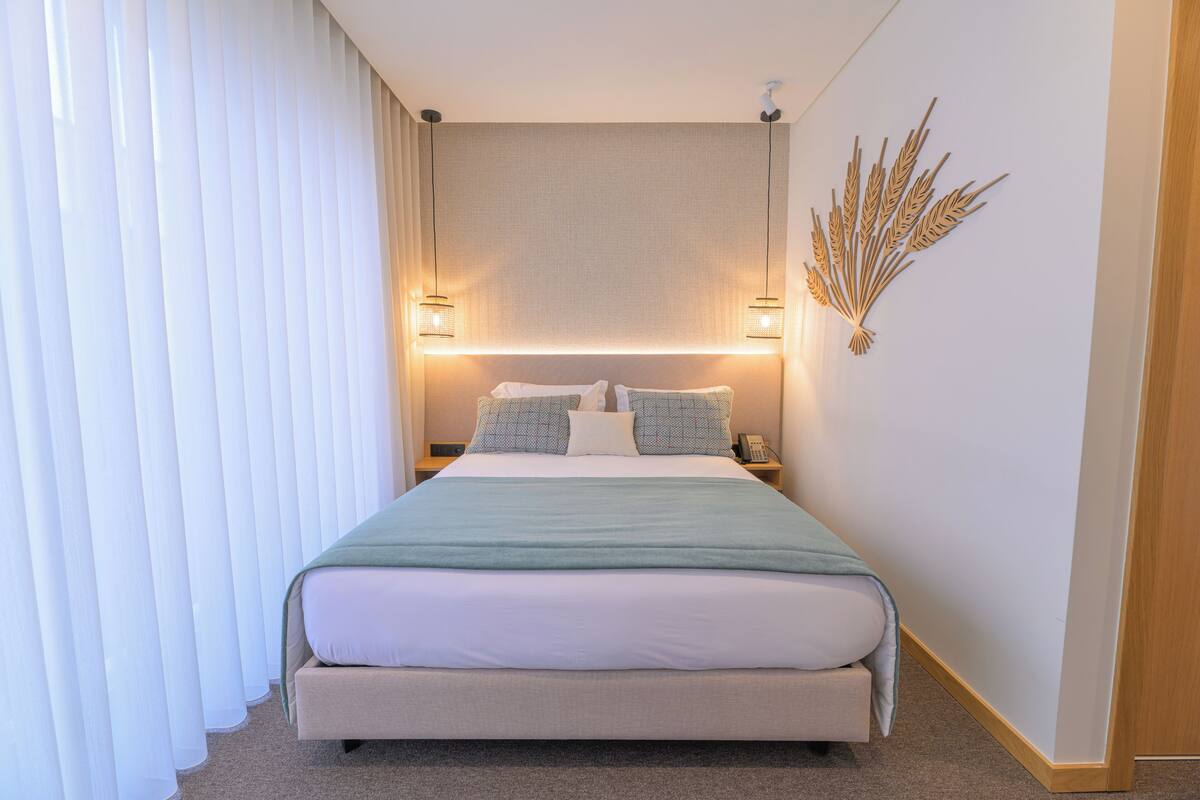 Un lit bien fait, recouvert d’une couverture verte, avec deux lampes de chevet et un élément décoratif fixé au mur.