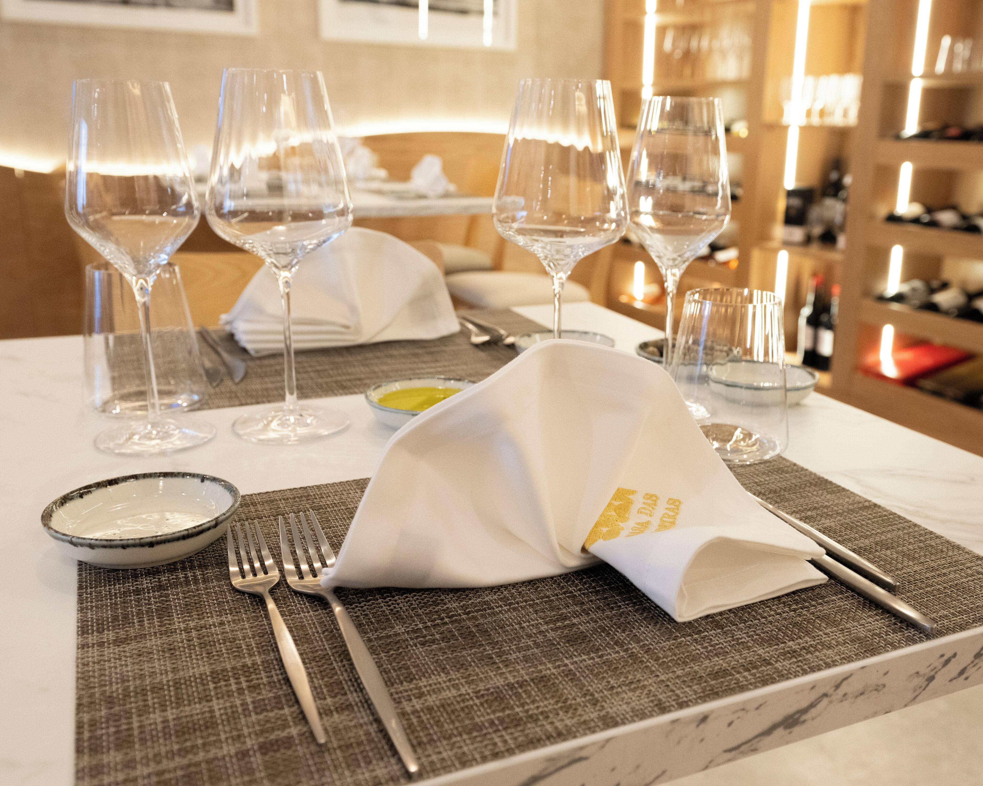 Une table dressée pour le repas, avec des verres à vin, une serviette pliée et des couverts.