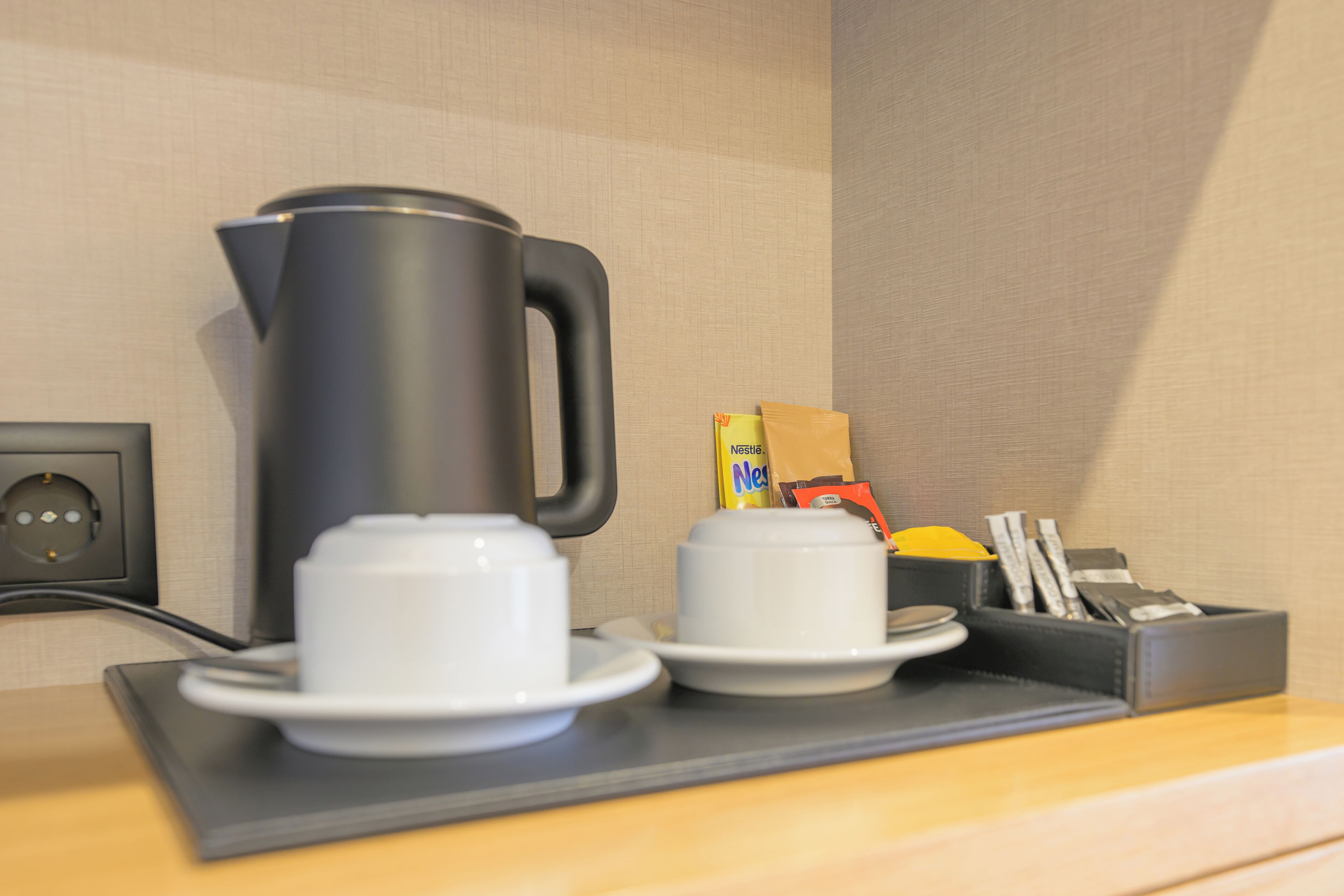 A coffee station with a coffee maker, cups, and a tray.