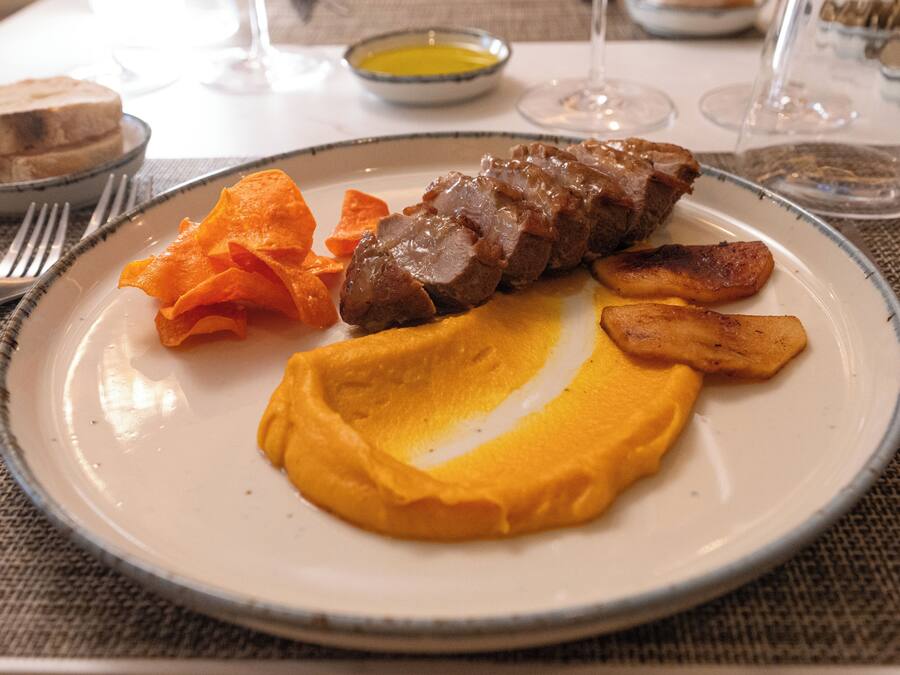 Un plato con una porción de carne, patatas asadas y puré de patatas.