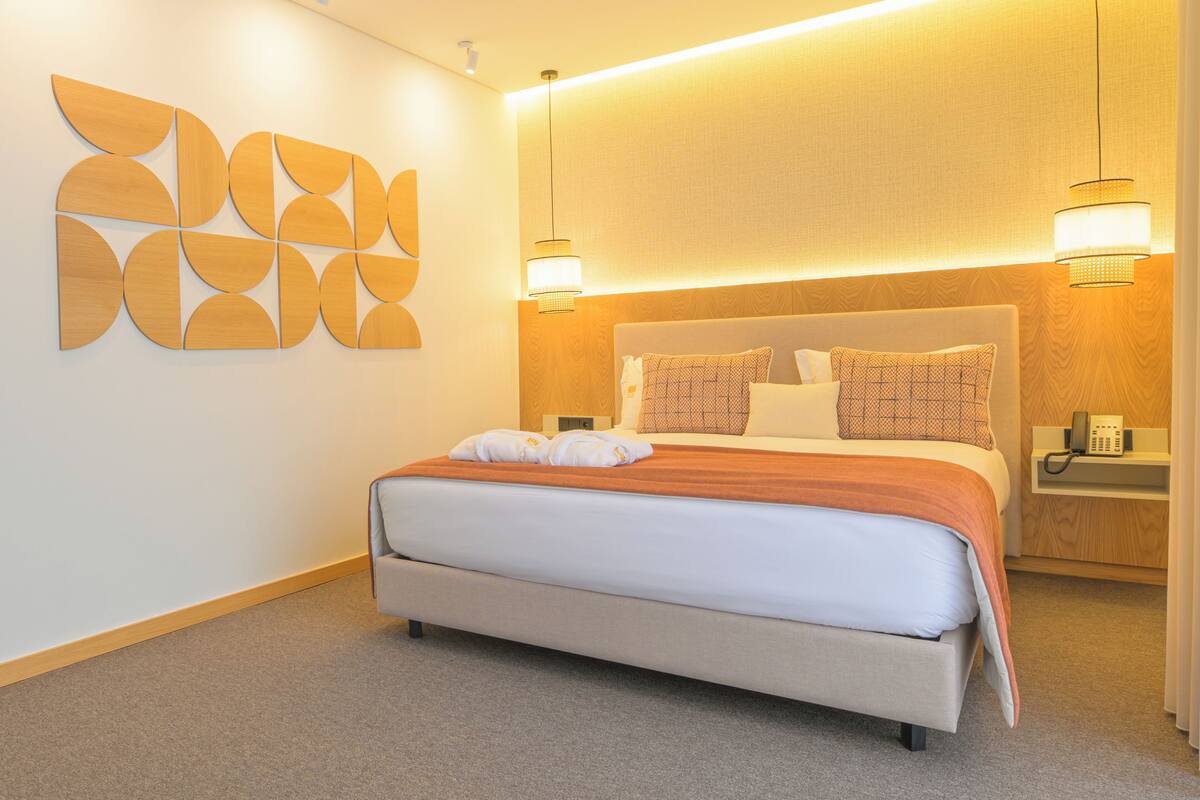 Une chambre d’hôtel moderne avec un grand lit, une tête de lit en bois et une œuvre d’art abstraite accrochée au mur.