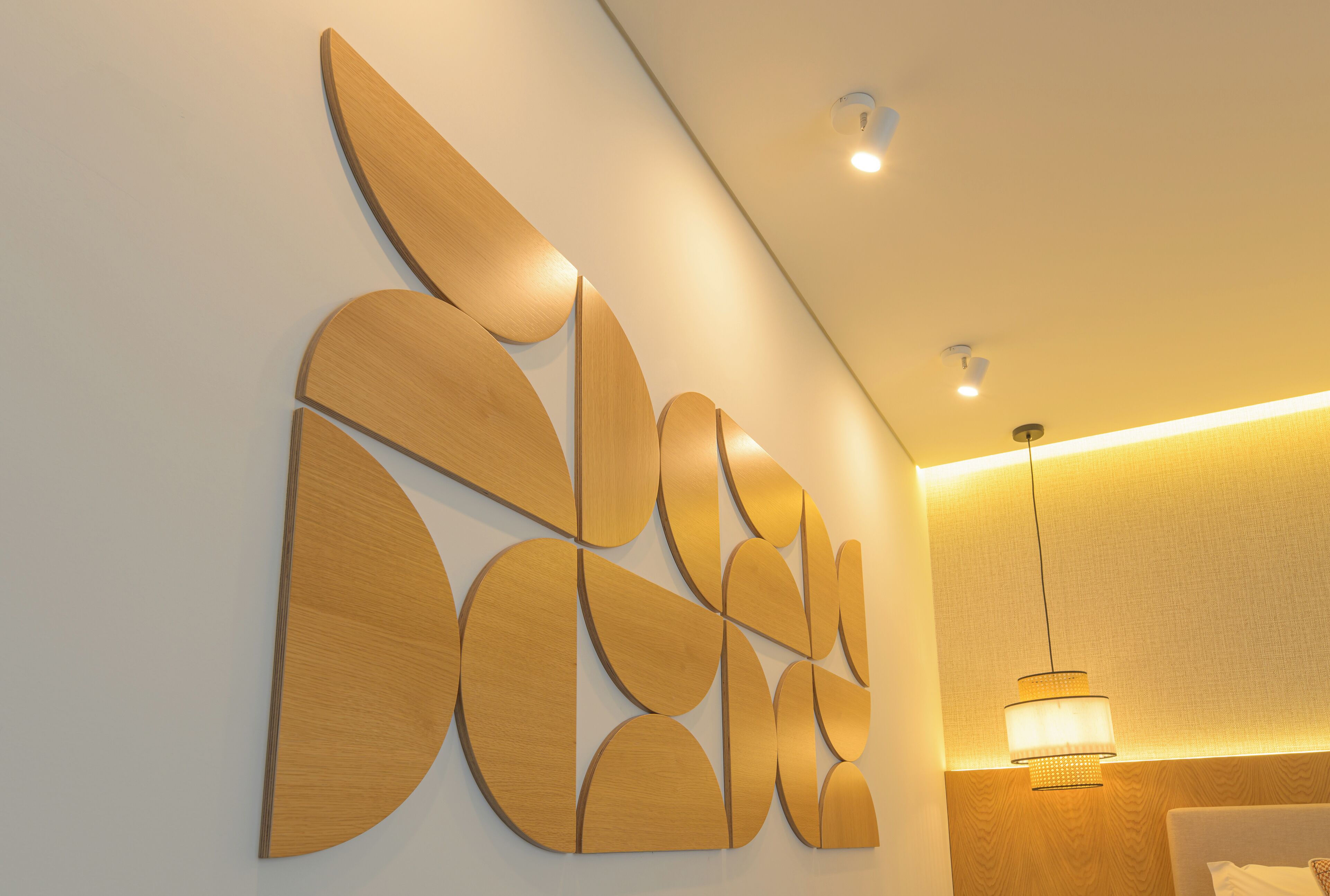 A modern hotel room with a wooden wall art piece, a bed, and a hanging light fixture.