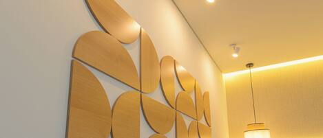 A modern hotel room with a wooden wall art piece, a bed, and a hanging light fixture.