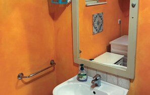 Een badkamer met een oranje wand, een witte wastafel, een spiegel en een handgreep.