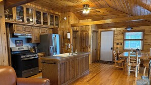 A wooden cabin interior with a kitchen, dining area, and seating.