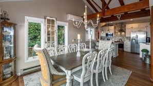 A dining area with a wooden table and white chairs, a chandelier, and a view of the kitchen. - Beech Mountain Retreat with Spectacular Panoramic Views (Banner Elk)