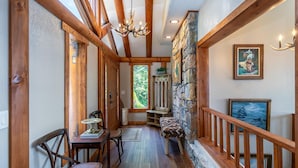 A wooden hallway with a stone wall, a bench, a table with chairs, and a chandelier. - Beech Mountain Retreat with Spectacular Panoramic Views (Banner Elk)