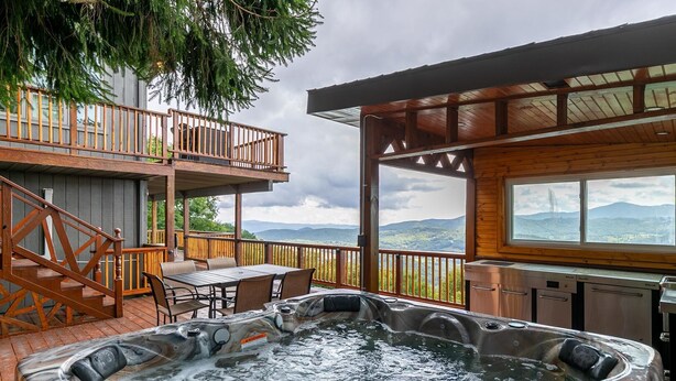 A hot tub on a wooden deck with a view of mountains, a covered outdoor seating area, and a staircase to an upper level. - Beech Mountain Retreat with Spectacular Panoramic Views (Banner Elk)