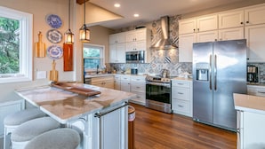A modern kitchen with white cabinetry, a central island, stainless steel appliances, and a decorative backsplash. - Beech Mountain Retreat with Spectacular Panoramic Views (Banner Elk)