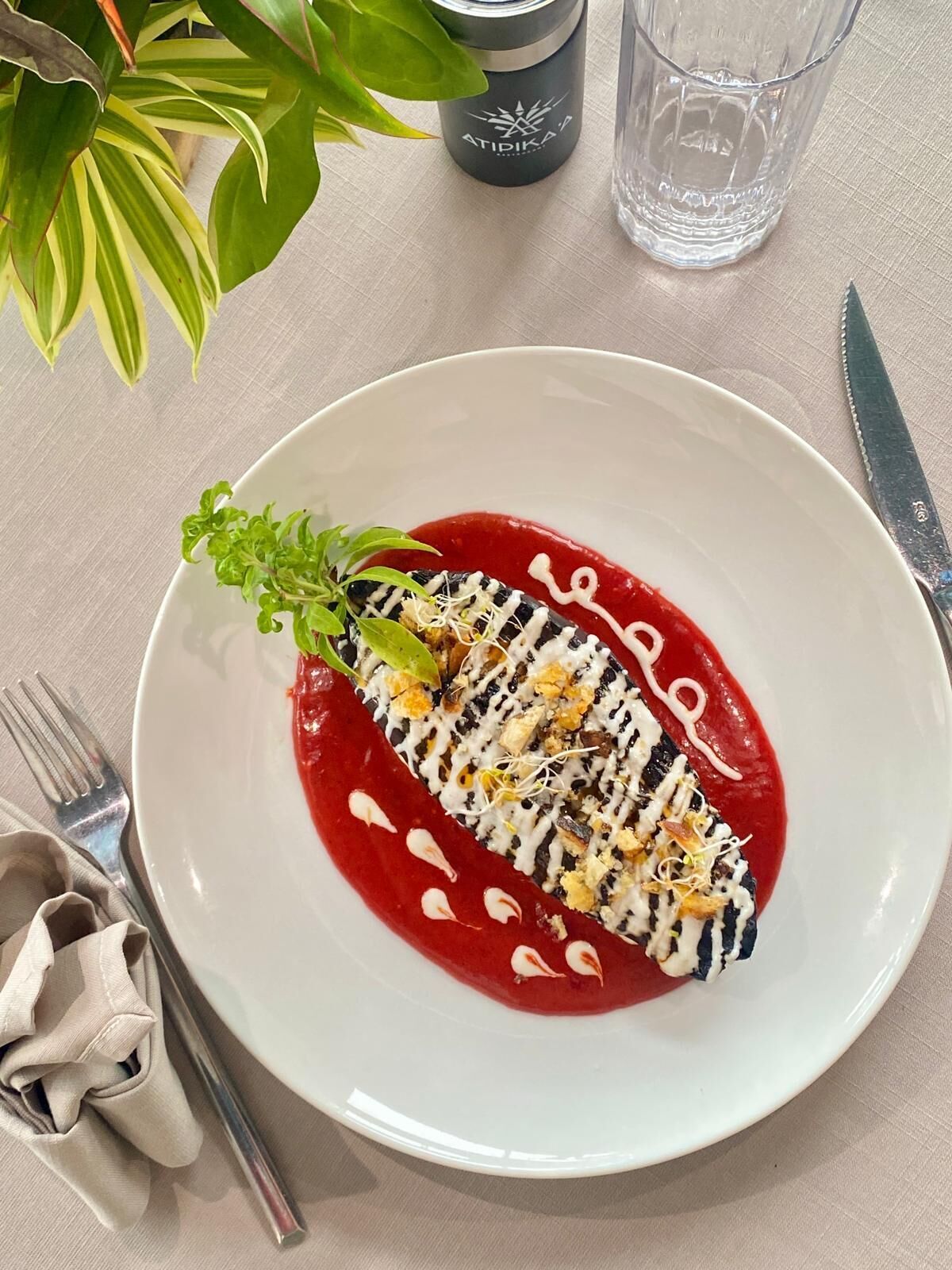 A plate with a food item, a glass of water, a knife, a fork, and a napkin on a table.