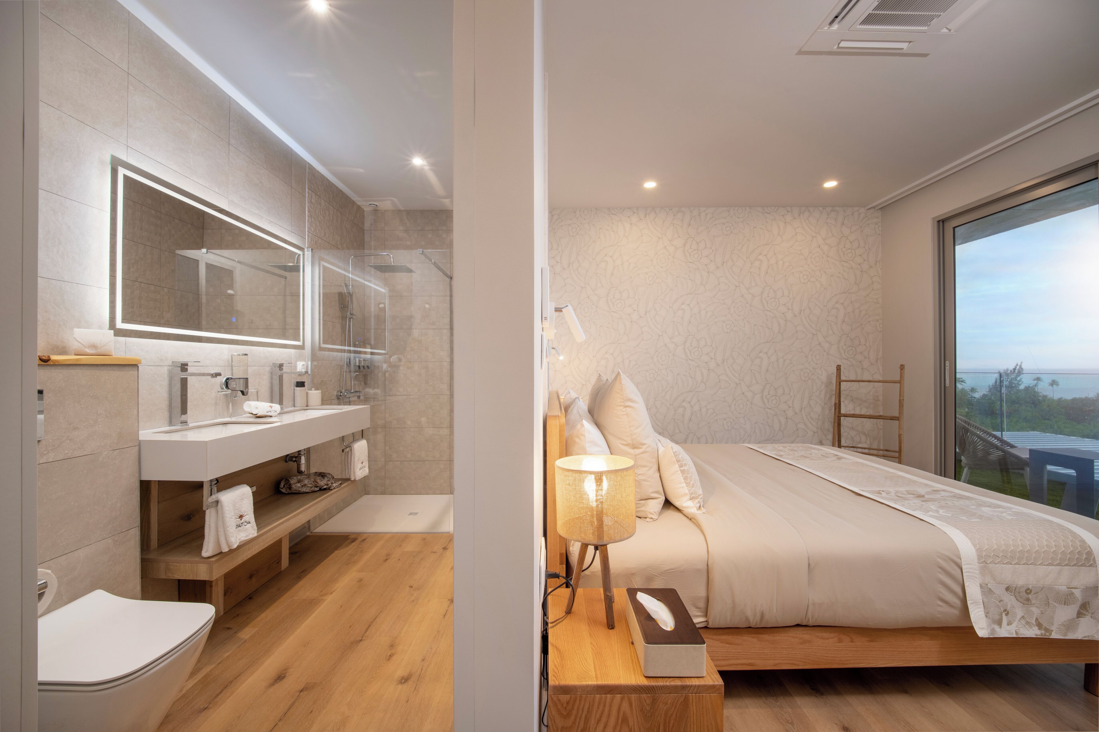 Un baño moderno con un espejo grande, un tocador y una ducha. El dormitorio tiene una cama, una mesita de noche y vistas al exterior.
