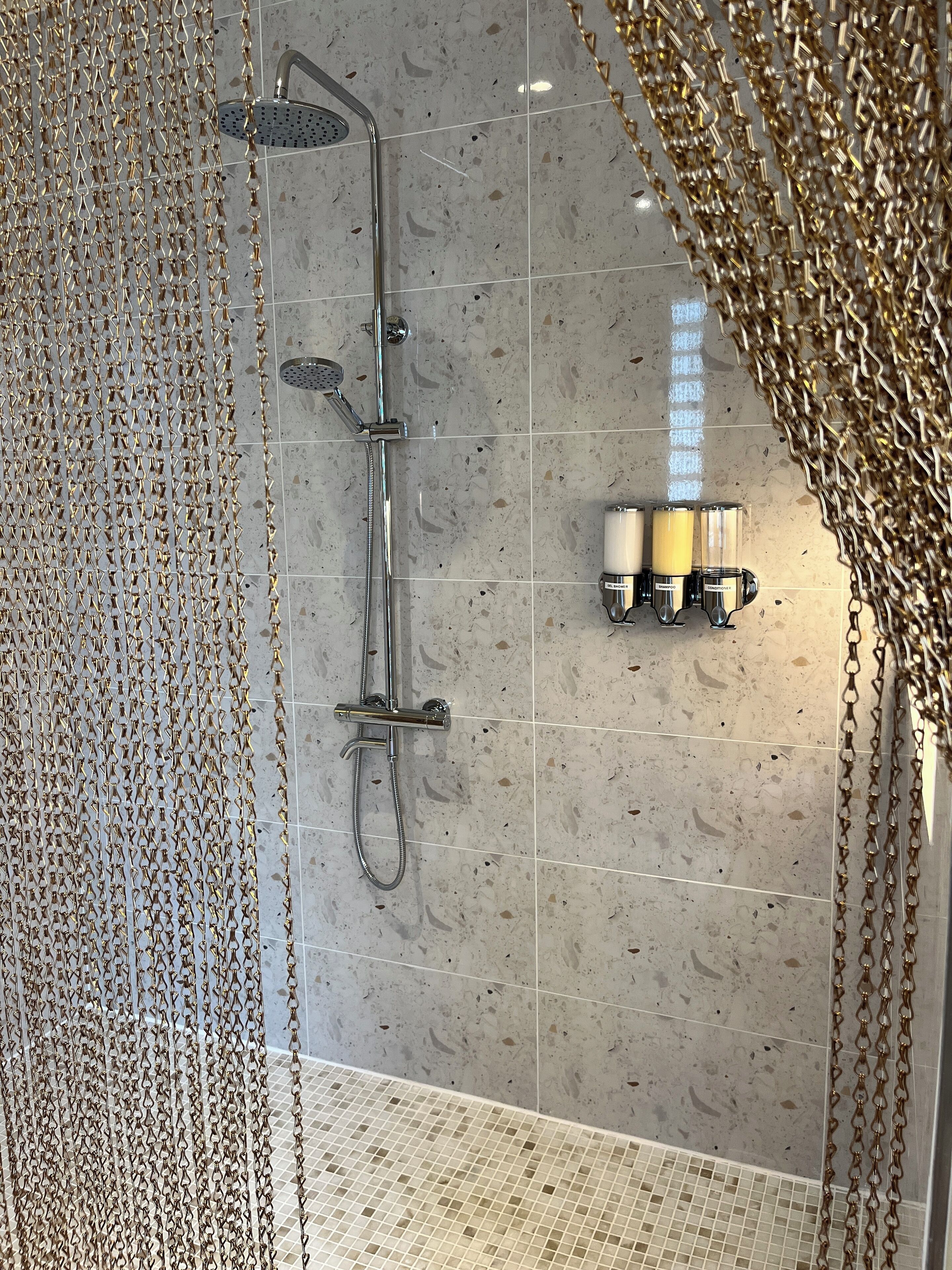 A shower with a rain showerhead and handheld showerhead, a glass door, and a tiled floor.