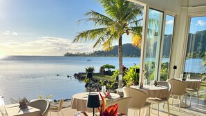 A restaurant with outdoor seating overlooking a body of water, featuring tables with chairs, a flower centerpiece, and a clear view of the landscape. - Apatoa Beach and Garden Village (Tumaraa)