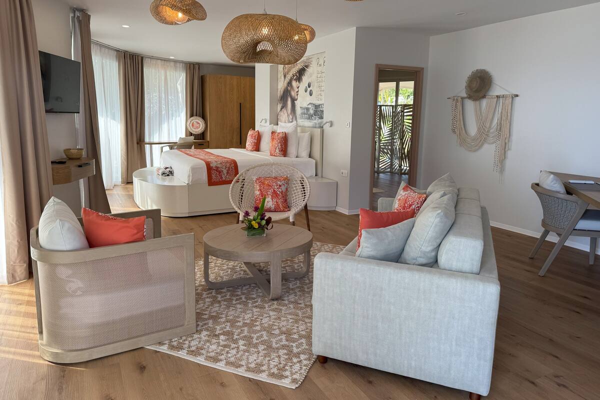 A modern living room with a sofa, chairs, a coffee table, and a bed with a red throw blanket.