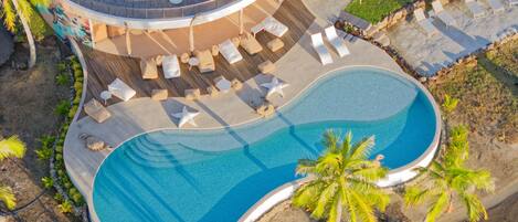 Luftaufnahme eines Resorts mit großem Pool, Liegestühlen und Palmen.