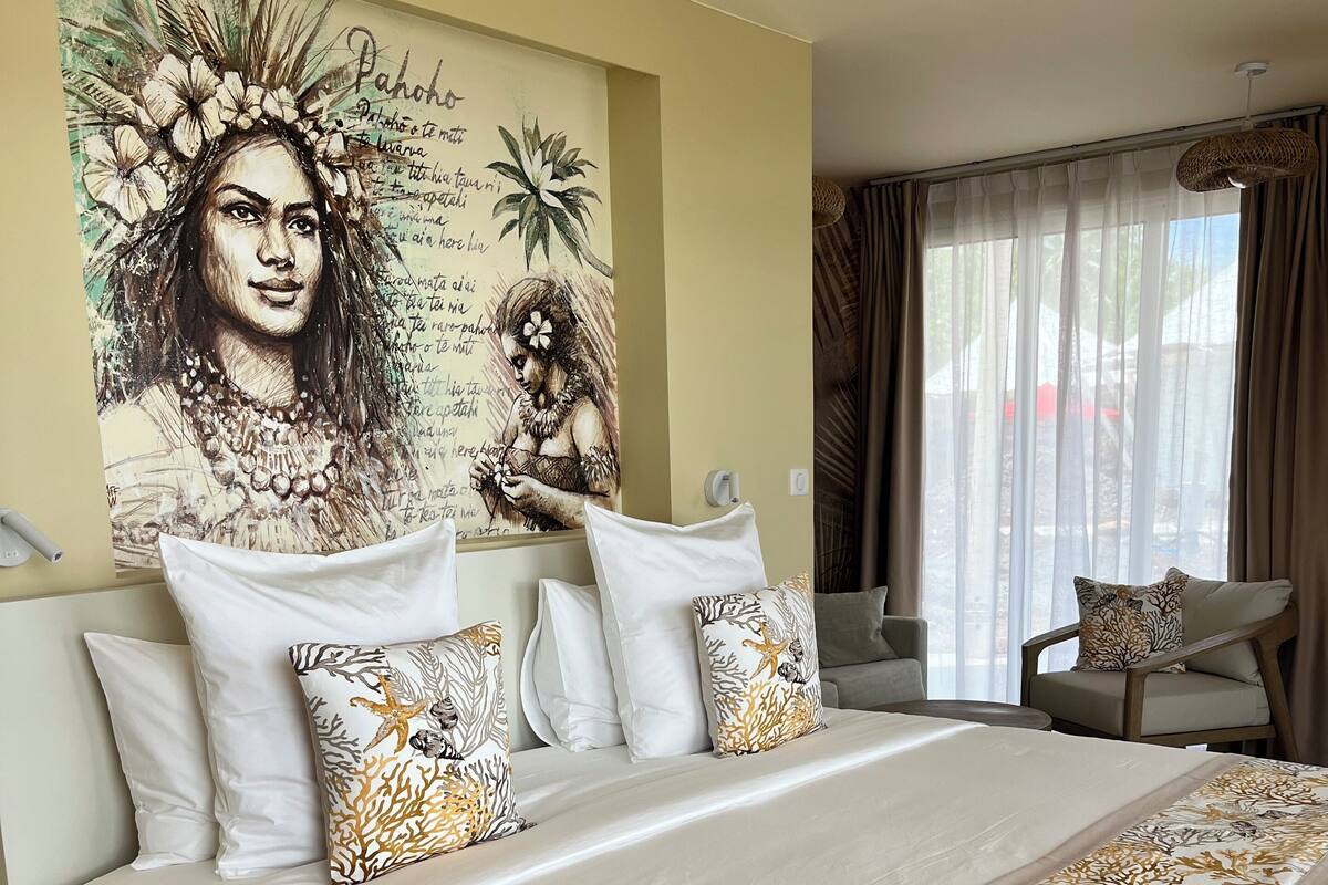 A bedroom with a large bed, white bedding, and a wall art piece.