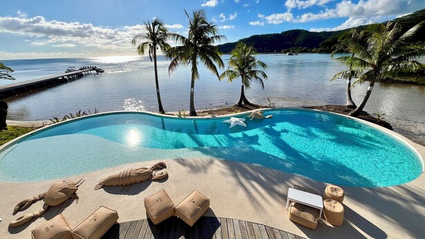 A pool with lounge chairs and a wooden deck overlooking a body of water with palm trees and a dock. - Apatoa Beach and Garden Village (Tumaraa)