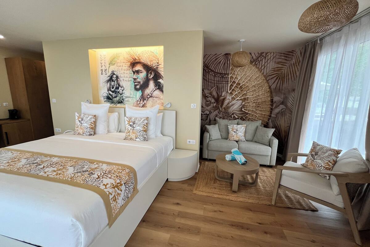A hotel room with a large bed, a sofa, a small table, and a decorative wall mural.