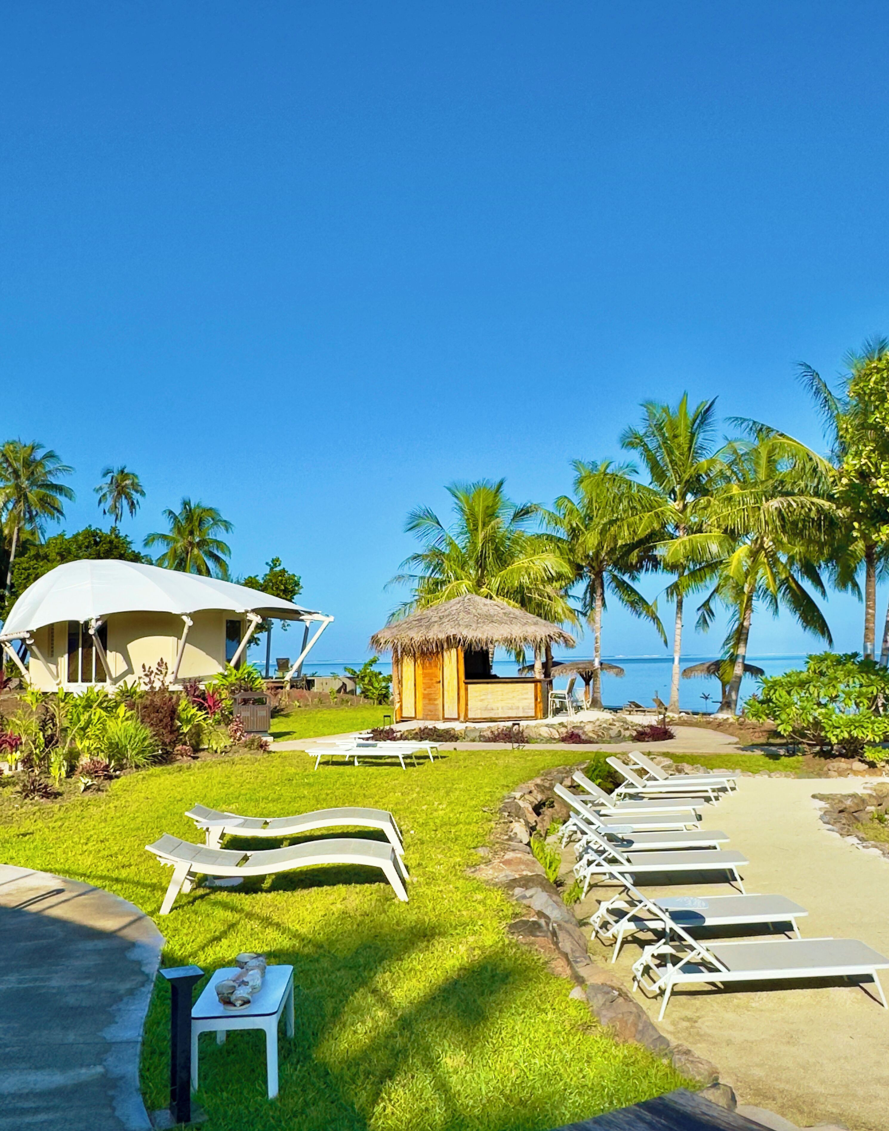 A resort with a pool, lounge chairs, a thatched hut, and palm trees.