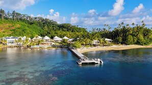 A resort with a dock extending into clear blue water, surrounded by lush greenery and palm trees. - Apatoa Beach and Garden Village (Tumaraa)