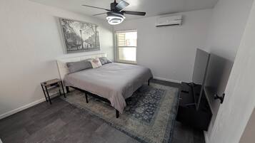 A bedroom with a bed, a ceiling fan, an air conditioner, a window, and a TV.