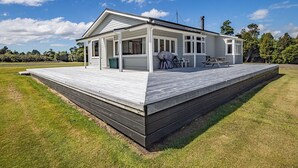 Una casa de un piso con porche cubierto, terraza y un pequeño espacio para sentarse al aire libre.